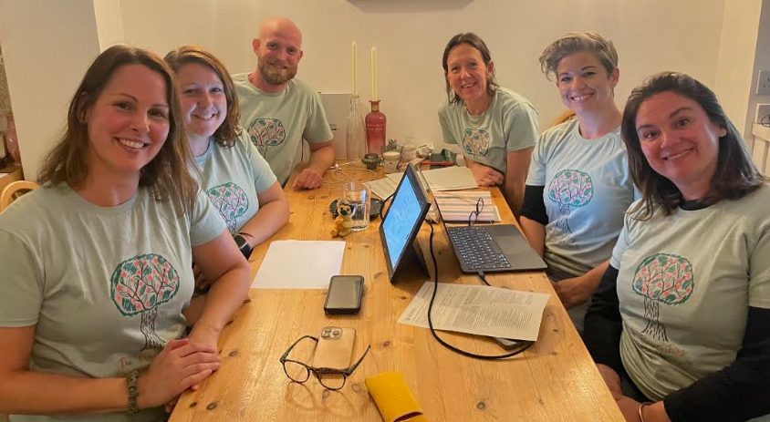 Flourishing trustees gathered around a table at their first trustee meeting, wearing matching Flourishing tree T-shirts